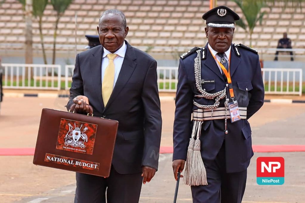 Matia Kasaija, Uganda’s Minister of Finance, carrying the "National Budget" briefcase alongside a police officer during the formal budget presentation.