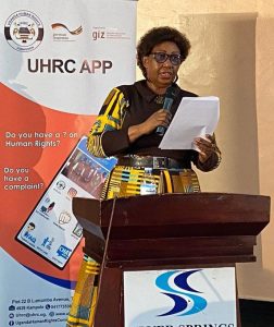UHRC Chairperson Mariam Wangadya speaking at a podium in front of a banner for the UHRC mobile app.