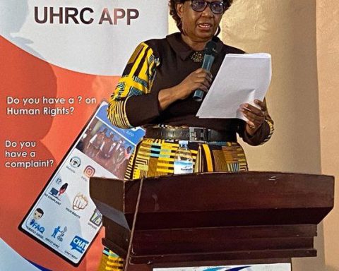 UHRC Chairperson Mariam Wangadya speaking at a podium in front of a banner for the UHRC mobile app.
